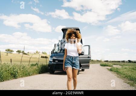 Besorgt junge afroamerikanische Frau mit lockigen Haaren reden auf dem Handy, während sie um Hilfe von Reparatur-Service nach Unfall mit Wohnmobil fragen Stockfoto