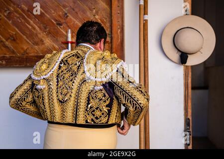 Rückansicht des anonymen Picador, der sich für den Stierkampf vorbereitet, indem er traditionelle glänzende Kostüme in einem Stall aufsetzt Stockfoto