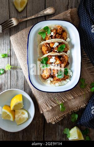 Von oben Blumenkohl Snack Tacos in Schüssel und Zitronenstücke in Teller auf Holztisch Stockfoto