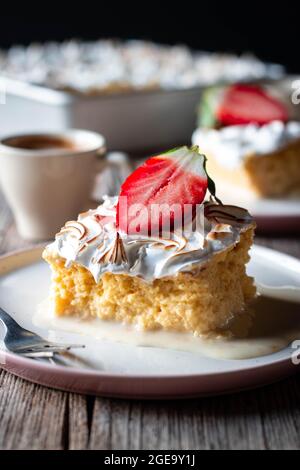 Süßer, köstlicher Kuchen aus drei Milchsorten mit halbfrischer Erdbeere auf weißem Teller auf Holztisch Stockfoto