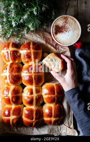 Von oben Erntegut Person Hand hält Brötchen auf dem Hintergrund des Tisches mit leckeren üppigen frisch gebackenen heißen Brötchen und eine Tasse Kaffee Stockfoto