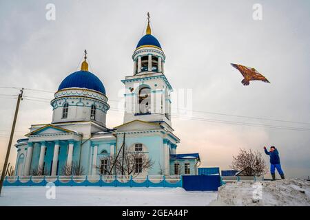 Ein Junge fliegt einen Drachen neben einer orthodoxen Kirche in einem kleinen Dorf im Uralgebirge in Russland. Stockfoto