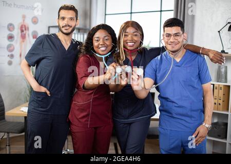 Krankenhauspersonal im modernen Zimmer. Internationales Ärzteteam oder Studentengruppe. Afrikanische und indisch-asiatische Ärzte mit gemischter Rasse zeigen ihre Stethoskope vor der Kamera und lächeln Stockfoto