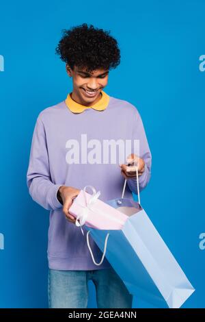 Fröhlicher afroamerikanischer Mann, der Geschenk in eine Papiertüte auf blauem Papier einlegt Stockfoto