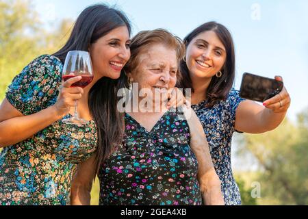 Großmutter und Enkelkinder, die ein Selfie auf einer Party machen, während sie Wein trinken. Neues normales Lifestyle-Konzept mit glücklichen Menschen, die gemeinsam Spaß haben, übertreffen Stockfoto