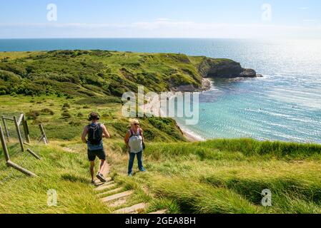 Mann, der einen steilen Hügel hinunterläuft, vorbei an einer Frau, die auf einem steilen Abschnitt des South West Coast Path in Lulworth Cove, West Lulworth, Dorset, Großbritannien, bergauf geht Stockfoto