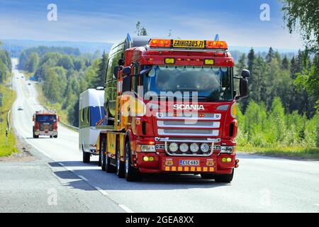 Scania Abschleppwagen der Serie 4 Erihinaus zieht Transporter und Wohnwagen in wunderschöner Landschaft auf dem Weg zur Power Truck Show 2021. Ikaalinen, Finnland. August 12, 2021. Stockfoto