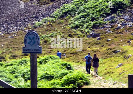 Junges Paar, das auf dem Weg durch den National Trust Wegweiser für „Anglers Crag“ in Ennerdale, Lake District National Park, Cumbria, England, Großbritannien, läuft. Stockfoto