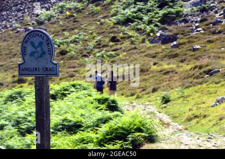 Junges Paar, das auf dem Weg durch den National Trust Wegweiser für „Anglers Crag“ in Ennerdale, Lake District National Park, Cumbria, England, Großbritannien, läuft. Stockfoto