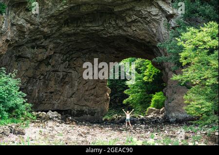 Blonde Frau, die unter der Natursteinbogenbrücke im Rakov Škocjan Landschaftspark steht Stockfoto