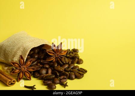 Aus einer kleinen Tüte verstreute Kaffeesorten liegen mit Anise und Zimt auf gelbem Hintergrund Stockfoto