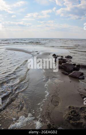 Fußabdrücke auf nassem Sand in der Nähe eines Steinstapels an der Küste mit einer Brandung gegen einen bewölkten Himmel Stockfoto