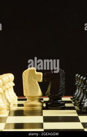 Auf einem Schachbrett sind weiße und schwarze Schachfiguren gegenübergestellt. Vorne sind die Figuren der Pferde, und hinter den Bauern. Hinter der Figur ist ein Stockfoto