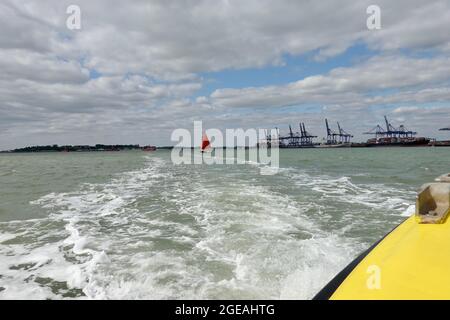 Harwich, Essex - 18. August 2021: Ein rot gesegeltes Segelschiff im Gefolge der Hafenfähre. Stockfoto