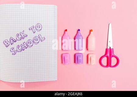 Zurück zur Schule. Komposition mit geöffnetem Copybook, Markern und Scheren auf rosa Hintergrund. Flach liegend. Konzept von Bildung und Kreativität. Stockfoto