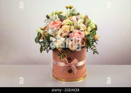 Ein schöner Strauß zarter Blüten aus rosa Rosen, weißen Lilien und gelben Gerberas in einer handgefertigten Schachtel. Alles ist mit grünen palmenlea dekoriert Stockfoto