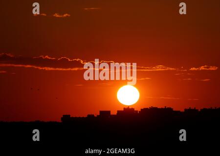 Sonnenuntergang über der Stadt, malerische Aussicht. Untergehende Sonne und orangefarbener Himmel mit dunklen dramatischen Wolken über schwarzen Silhouetten von Wohngebäuden Stockfoto