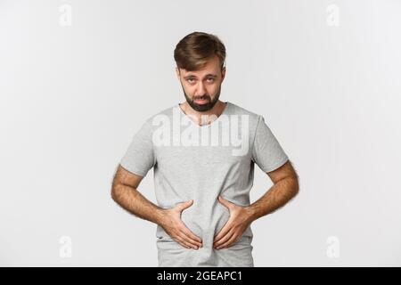 Portrait von Kerl Gefühl aufgeregt über sein Gewicht, zeigt Fett auf Bauch und sieht enttäuscht, schmollend wie über weißem Hintergrund Stockfoto