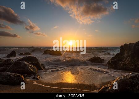 Ein wunderschöner goldener Sonnenuntergang mit Spiegelungen auf den Wellen, die über dem Strand schwaden und der Sonnenuntergang hinter dem Horizont. Stockfoto