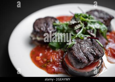 Nahaufnahme von Fleischrindmedaillon auf Tomate und gegrillter Aubergine mit Salsa-Sauce Stockfoto