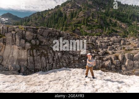 Kleiner Junge wirft Schneebälle im Sommer auf Heather Meadows im Mt. Baker-Snoqualmie National Forest. Stockfoto