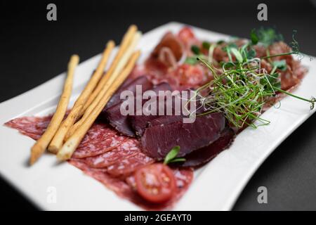 Kalte Fleischplatte mit Salami, Prosciutto und Brotstäbchen auf schwarzem Hintergrund Stockfoto