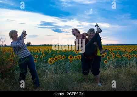 Drei Freundinnen mittleren Alters scherzen, amüsieren sich und lachen in einem Sonnenblumenfeld Stockfoto