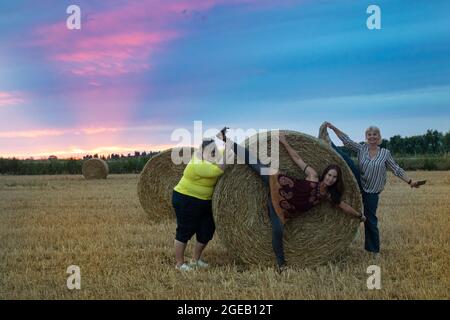 Drei Freundinnen mittleren Alters scherzen, haben Spaß und lachen auf einem Feld mit Heuhaufen Stockfoto