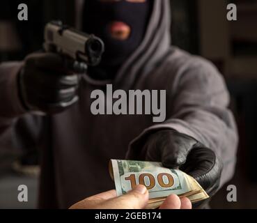 Räuber in einer Sturmhaube droht mit einer Waffe für den Diebstahl von Geld, bewaffneter Raub, Schütze mit einer Pistole in der Hand mit Handschuhen, Nahaufnahme. Stockfoto