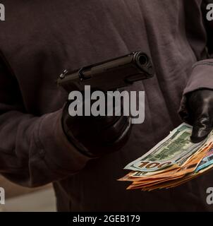 Dieb droht mit einer Pistole, weil er Geld gestohlen hat, Nahaufnahme. Bewaffneter Raub, Mann mit Waffe und Geldscheinen in Handschuhen, Stockfoto