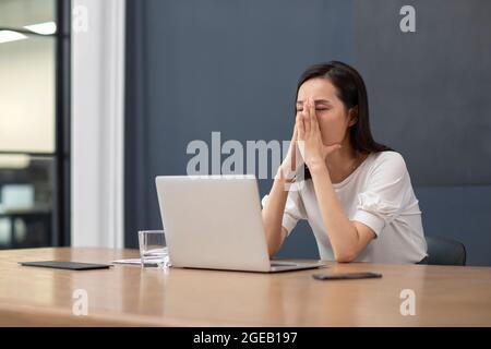 Chinesische Geschäftsfrau frustriert durch schlechte Nachrichten am Schreibtisch Stockfoto