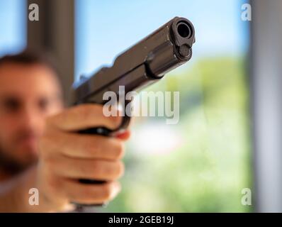 Pistole in männlicher Hand. Mann, der mit einem Gewehr anvisieren wollte, verwackelte Glasfenster im Hintergrund, Nahaufnahme. Killer, Mörder und Selbstverteidigungskonzept Stockfoto