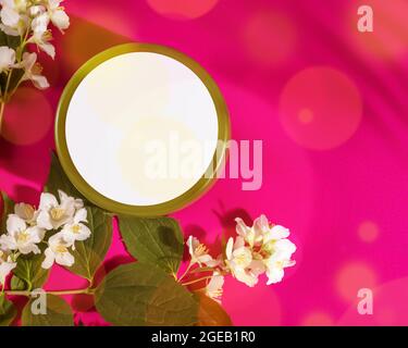 Cremedose für dein Design Mock Up. Spa, entspannen Sie die tropische Komposition mit einem Naturkosmetikprodukt in einem runden Glas und jasmin-Blüten auf einem rosa Hintergrund Stockfoto