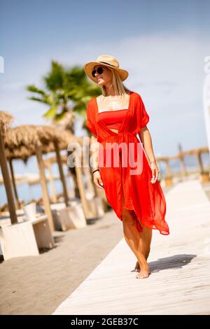 Hübsche junge Frau in rotem Kleid, die im Sommer am Strand spazieren geht Stockfoto