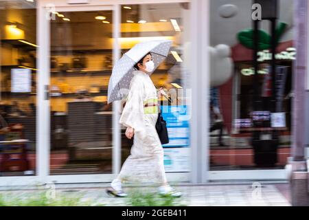 Eine Japanerin, die in einem traditionellen Kimono gekleidet ist, geht eine Straße im historischen Asakusa-Viertel in Tokio, Japan, entlang. Stockfoto