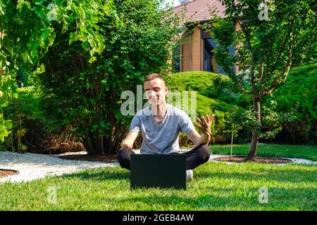 Kerl mit amputierten Arm sitzt auf dem Rasen und im Gespräch mit Freunden über soziales Netzwerk Stockfoto