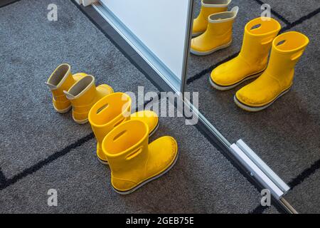 Nahaufnahme der gelben Gummistiefel für Kinder auf einer Matte in der Nähe eines Schranks mit einem Spiegel im Flur. Kinderschuhe Konzept. Schweden. Stockfoto