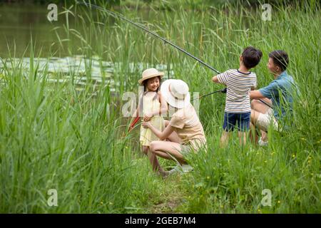 Glückliche junge chinesische Familie, die am Fluss fischt Stockfoto