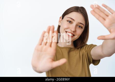 Porträt eines lächelnden Mädchens, das durch ihre Hände schaut, die Arme in der Geste des Kamerabildes ausstreckt, sich ein Bild von Smeth macht, den Moment einfängt, über Weiß steht Stockfoto