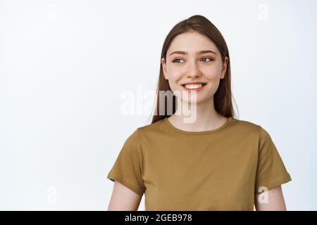 Bild einer jungen hoffnungsvollen Frau, die glücklich lächelt und auf leeren Raum für Banner, Verkaufswerbung schaut, die auf weißem Hintergrund steht Stockfoto