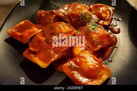 Traditionelle italienische Ravioli gefüllt mit Ricotta-Käse, serviert mit Tomatensauce und Basilikumblättern auf einem schwarzen Teller Stockfoto