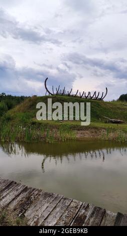 Holzskelett am grünen Hügel in der Nähe eines ruhigen Sees. Stockfoto