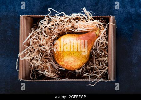 Helle, reifen, saftigen orange Birne Berra in einem Handwerk Karton im Heu. Umweltfreundliche Verpackung ohne Kunststoff. Gelbe Birne in eine Box auf einem dunklen zurück Stockfoto