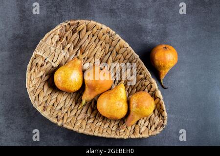 Orange Birnen in einem Weidenkorb und auf einem grauen Tabelle Reif. Platz für Text. Zusammensetzung der Weidenkörbe aus Palmblättern mit gelben Birnen. Gesunde fres Stockfoto