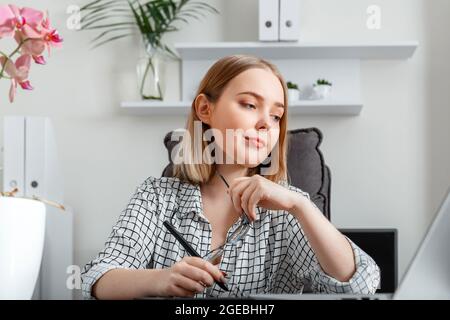 Junge freiberufliche Grafikdesignerin, die im Home-Office-Bereich mit einem grafischen Tablet und einem Laptop arbeitet. Kaukasische Blonde selbstbewusst fokussierte Frau tut Stockfoto