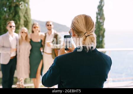 Der Mann im Anzug schießt eine Gruppe von Menschen auf einem Smartphone vor dem Hintergrund des Meeres Stockfoto