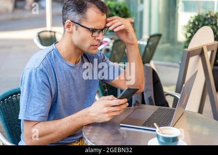 Der junge latein betonte, draußen mit Handy und Computer zu arbeiten. Stockfoto