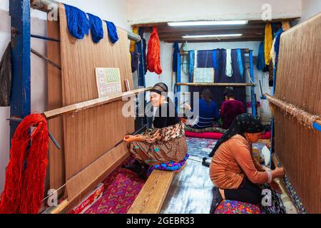 Chiwa, Usbekistan - 15. April 2021: Einheimische Frauen weben einen traditionellen usbekischen handgefertigten Teppich in der Stadt Chiwa, Usbekistan Stockfoto