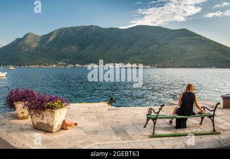 Eine junge Frau sitzt auf einer Bank am Wasser mit Blick auf die Bucht von Kotor am beliebten Touristenziel. Stockfoto