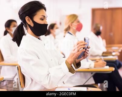 Asiatische Ärztin in Schutzmaske mit Smartphone auf dem medizinischen Kongress Stockfoto